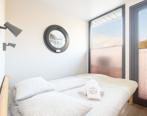 Przytulny pokój hotelowy z podwójnym łóżkiem, okrągłym oknem i dużym przeszkleniem z widokiem na zewnątrz.