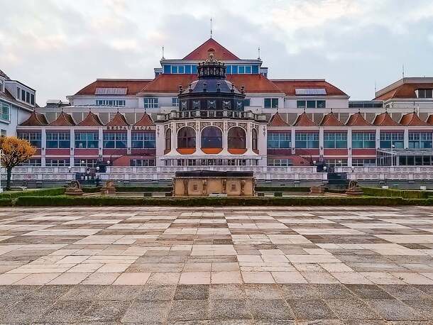 Nadmorski hotel z restauracją, ozdobnym centralnym pawilonem, czerwonymi dachami, tarasem, fontanną i promenadą z drzewami
