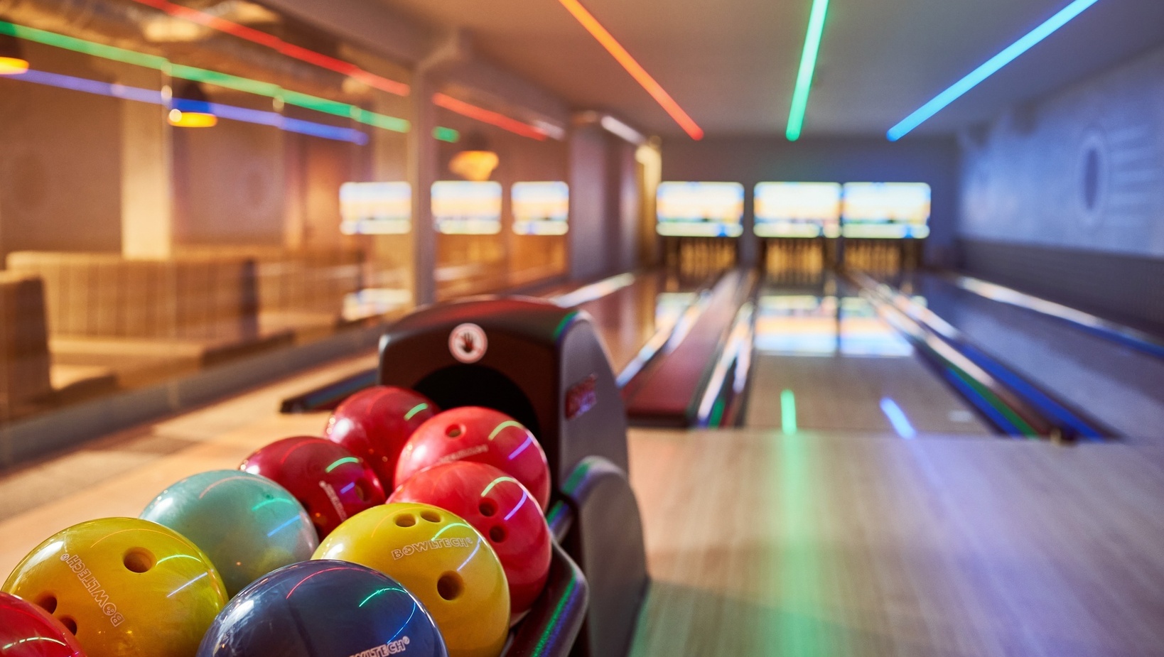 Hotelowy tor kręglarski z kolorowymi kulami, neonowym oświetleniem sufitowym i wygodnymi lożami w tle.
