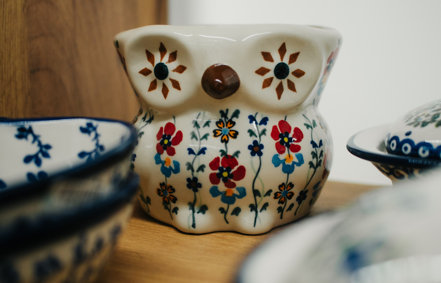 Ceramiczna sowa-miska z ludowym, kolorowym wzorem kwiatowym na drewnianej półce obok misek.
