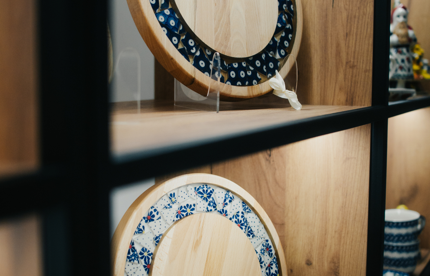Drewniane deski do serwowania z niebieskim ceramicznym ornamentem, ekspozycja na drewnianej półce z ciepłym oświetleniem