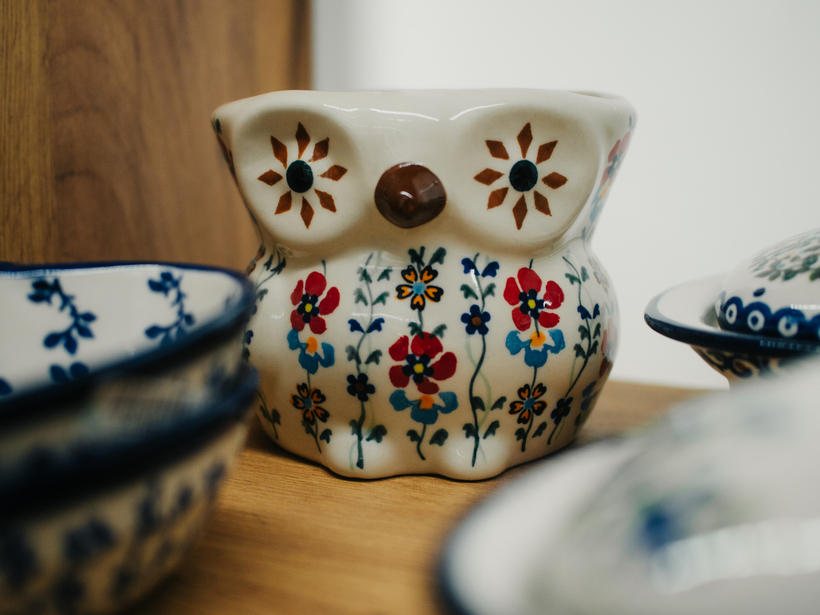Ceramiczna sowa-miska z ludowym, kolorowym wzorem kwiatowym na drewnianej półce obok misek.