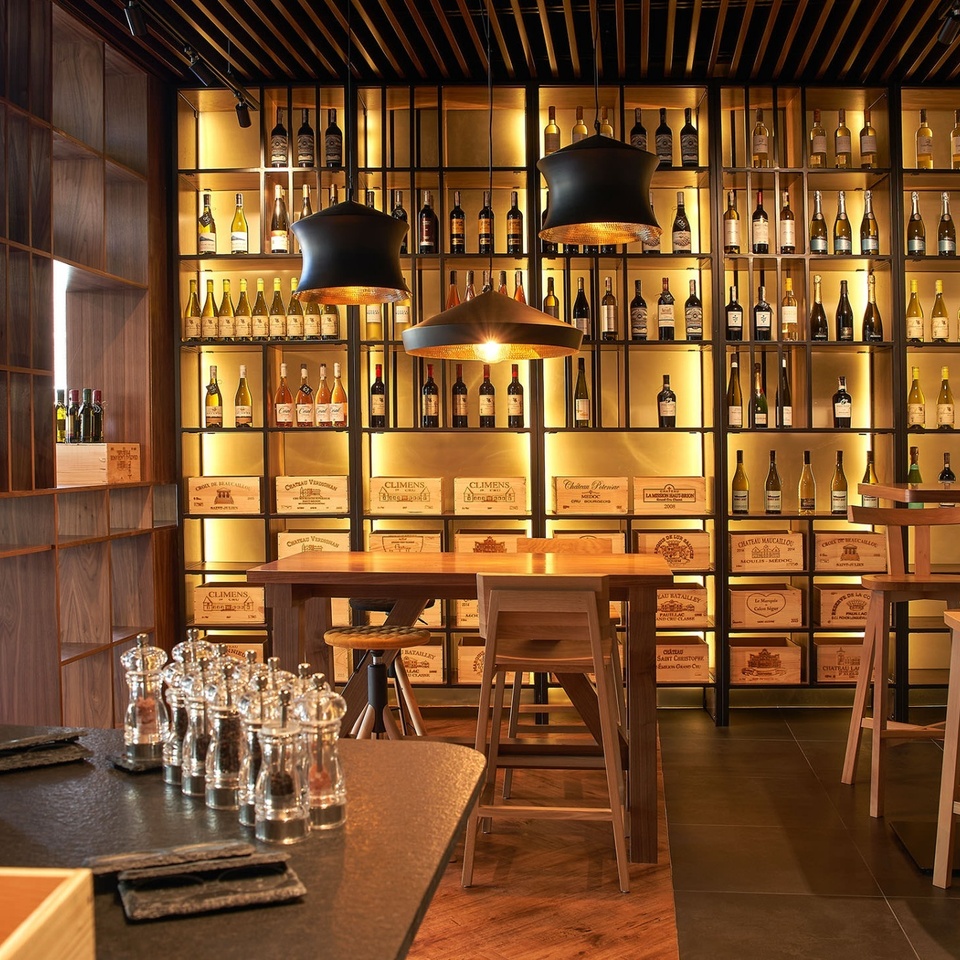 Elegancki bar i winiarnia hotelowa z drewnianymi regałami pełnymi butelek, podświetlonymi skrzyniami wina, stołem, hokerami i wiszącymi lampami.