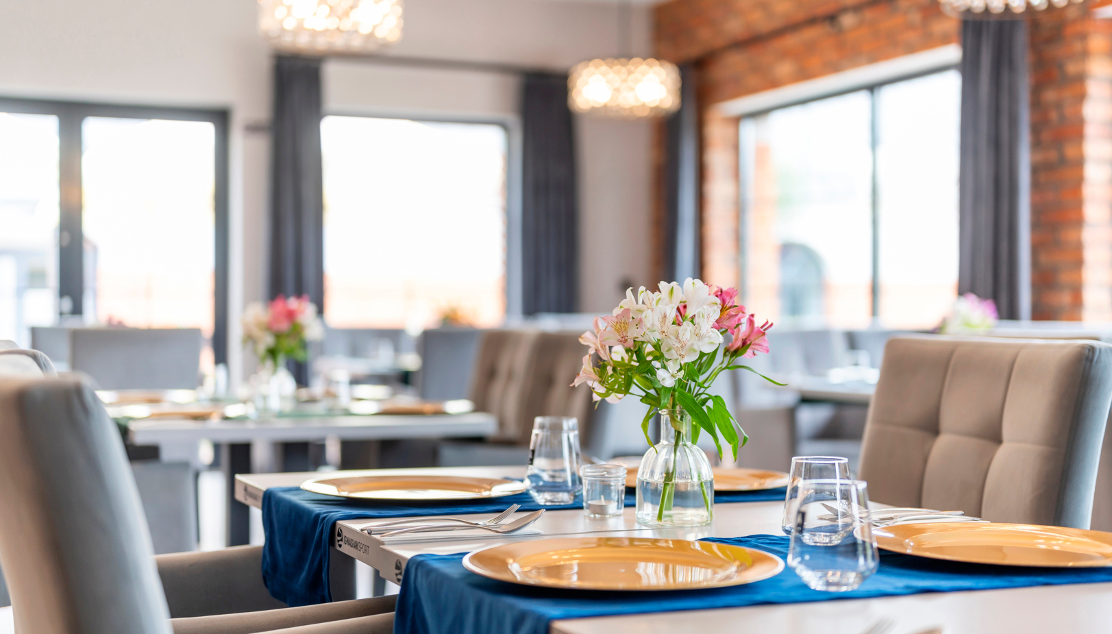 Nowoczesna restauracja hotelowa, stół przygotowany na kolację: złote podtalerze, niebieskie bieżniki, szkło i świeży bukiet.