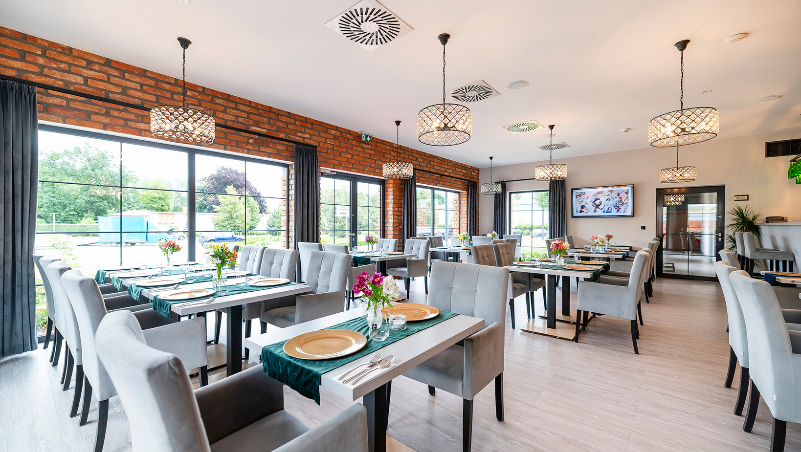 Restauracja hotelowa z ceglaną ścianą, kryształowymi lampami, dużymi oknami i nakrytymi stolikami z tapicerowanymi krzesłami