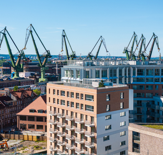 Nowoczesny hotel z balkonami i tarasem na dachu, z widokiem na czynny port i panoramę miasta.
