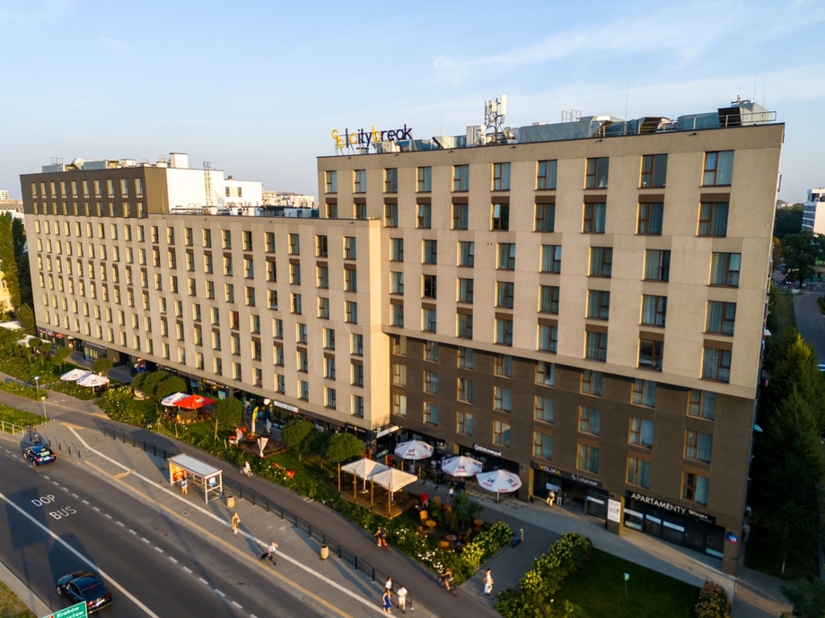 Nowoczesny miejski hotel z wieloma oknami, kawiarniami na parterze i tarasem z parasolami przy przystanku