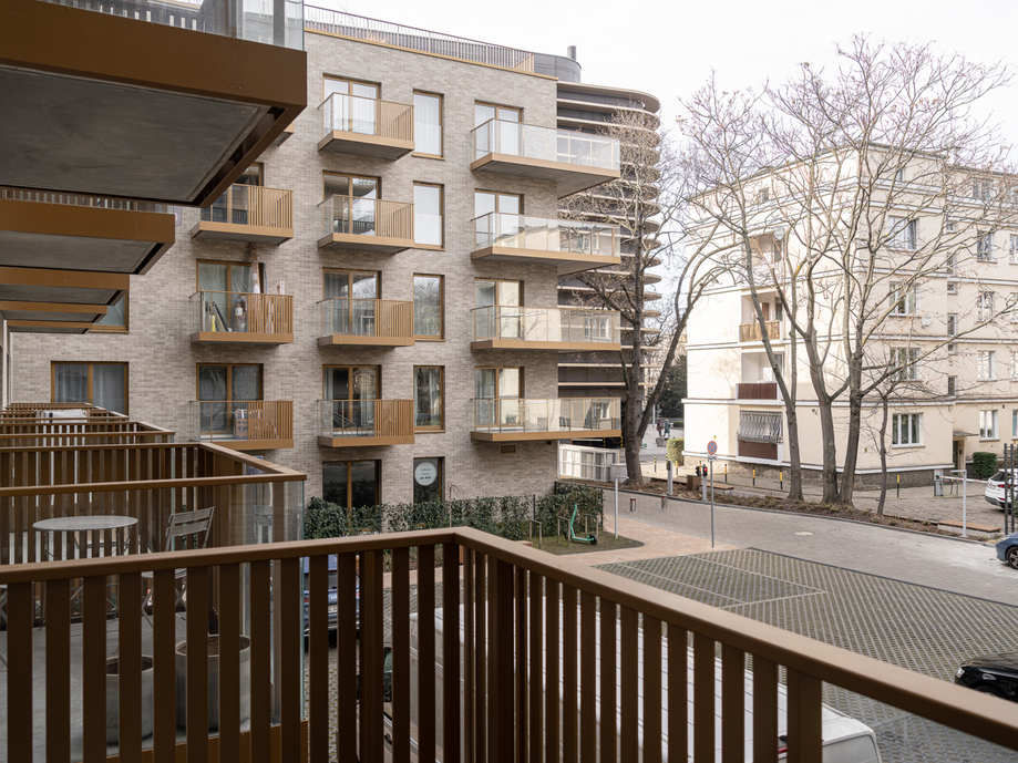 Courtyard view of modern hotel with brick facade, private balconies with bistro tables, street parking and bare trees.