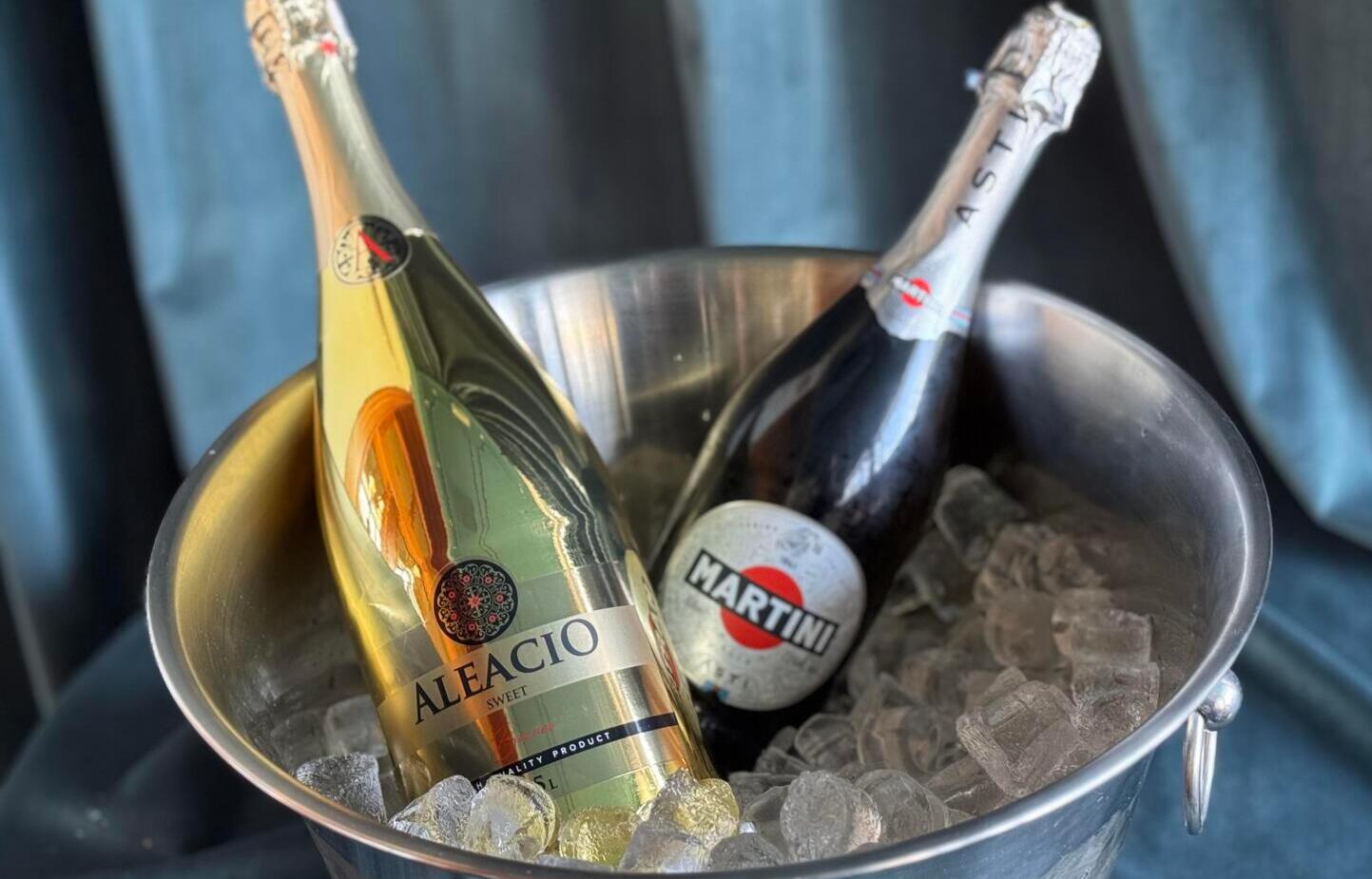 Dwie butelki prosecco, Aleacio Sweet i Martini Asti, schłodzone w metalowym wiadrze z lodem, gotowe na przyjęcie.