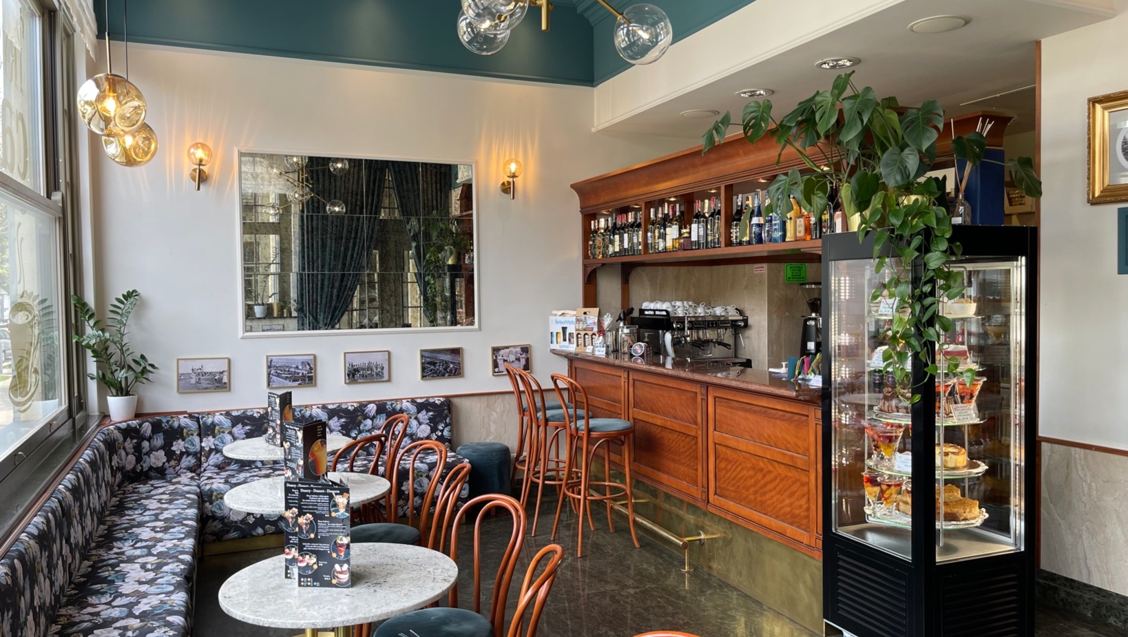 Przytulna kawiarnia w hotelu Irys w Świnoujściu z granitową podłogą drewnianymi krzesłami i barem z wystawionymi butelkami alkoholi oraz lodówką pełną przepysznych deserów
