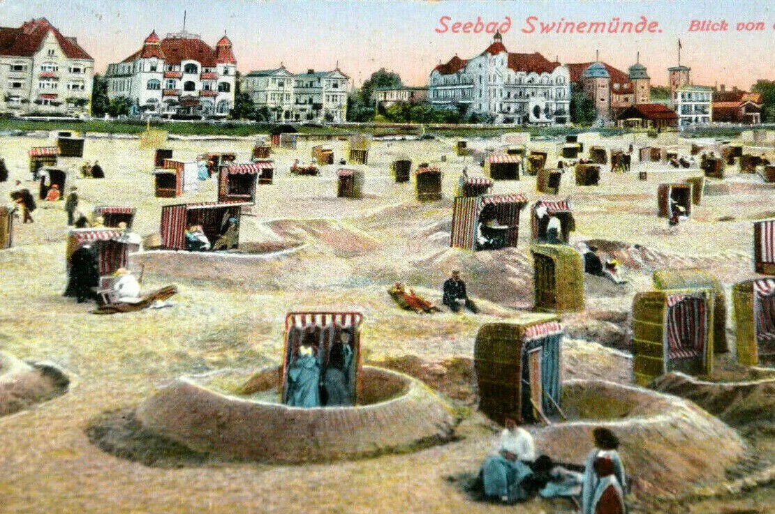 Historyczne nadmorskie kąpielisko w Świnoujściu z pruskimi koszami plażowymi i zabytkowymi budynkami w tle.