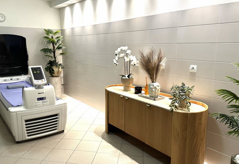 Prywatny pokój spa z kapsułą hydroterapeutyczną, nastrojowym oświetleniem i drewnianą komodą ze storczykami i roślinami