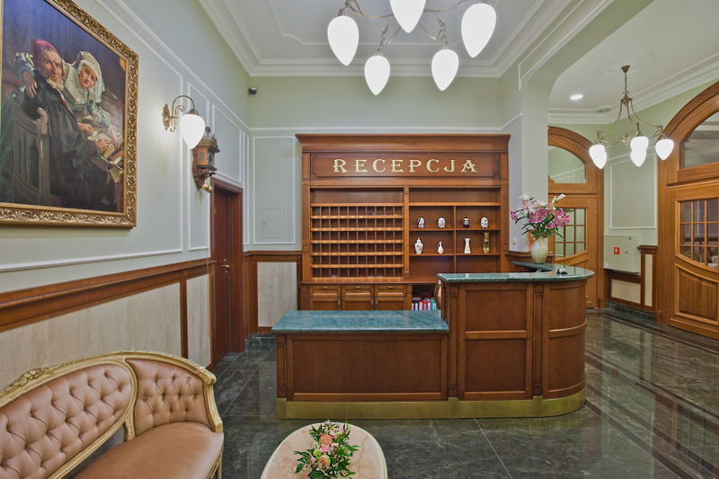 Klasyczna recepcja hotelowa z drewnianym biurkiem, zielonym marmurowym blatem i wygodną sofą w stylu vintage.