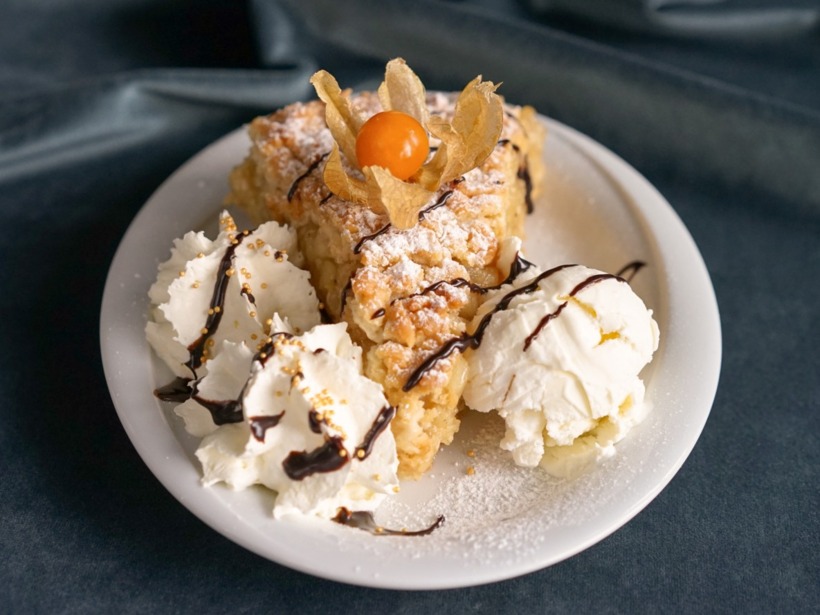 Porcja ciasta z owocem physalis, podana z bitą śmietaną i gałką lodów, polane czekoladą na białym talerzu.