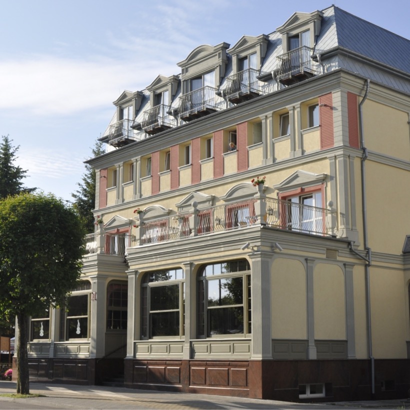 Hotel z klasyczną architekturą, trzypiętrowy budynek z balkonami i dużymi oknami na słoneczny dzień