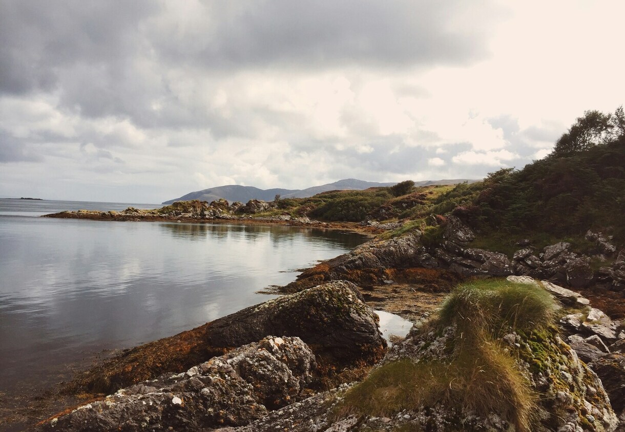 Secluded rocky coastal cove with calm sea, grassy cliffs and moody overcast sky — peaceful seaside setting for a coastal retreat.