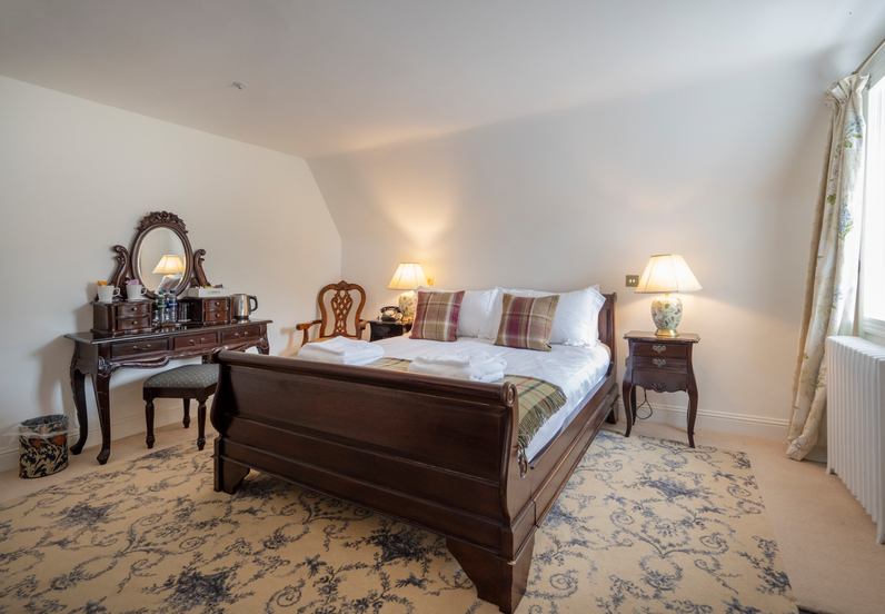Elegant double room with dark-wood sleigh bed, plaid pillows, bedside lamps, antique vanity with tea, chair and patterned rug