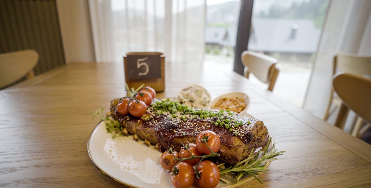 Talerz z żeberkami z sosem, świeżymi pomidorkami koktajlowymi i ziołami podany na drewnianym stole w przytulnej jadalni.