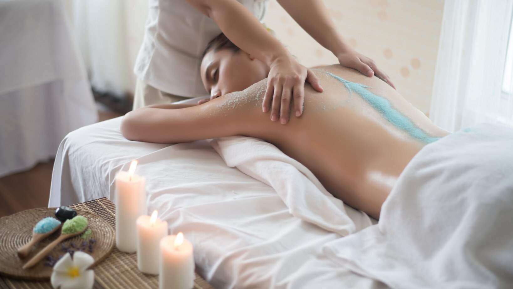 Relaksujący masaż pleców ze złuszczającym peelingiem w spa, świece i naturalne kosmetyki tworzą spokojną atmosferę