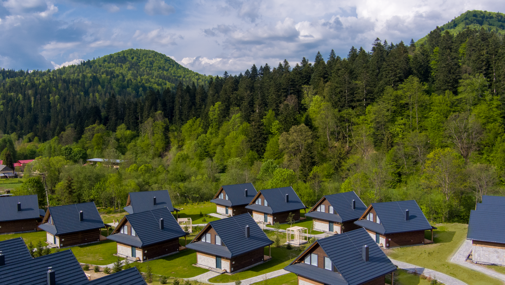 Nowoczesne drewniane domki letniskowe z kamiennymi elewacjami pośród zielonych wzgórz i gęstego lasu