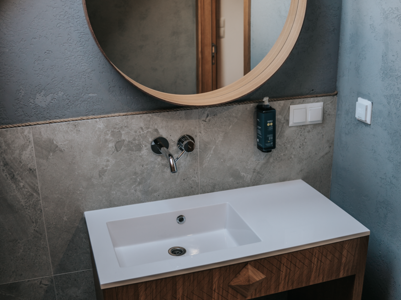 Nowoczesna łazienka z okrągłym drewnianym lustrem, umywalką osadzoną na drewnianej szafce i miękkim ręcznikiem.