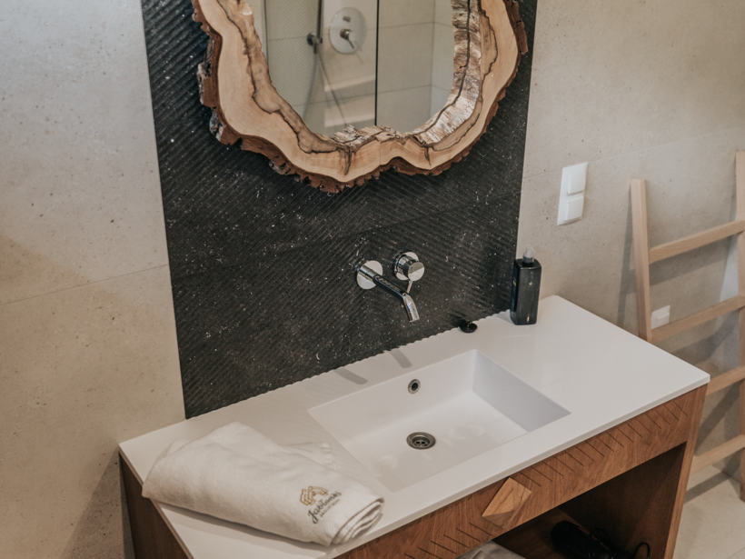 Nowoczesna łazienka hotelowa z drewnianą toaletką, unikalnym lustrem z naturalnego drewna i białą umywalką.