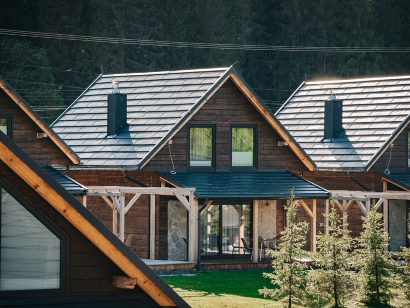 Drewniane domki z dwuspadowym dachem i tarasami zewnętrznymi, ogród z młodymi drzewkami i leśne otoczenie