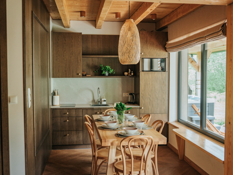 Przytulna jadalnia z nowoczesną kuchnią w drewnie, dużym stołem na sześć osób i widokiem na ogród przez okno