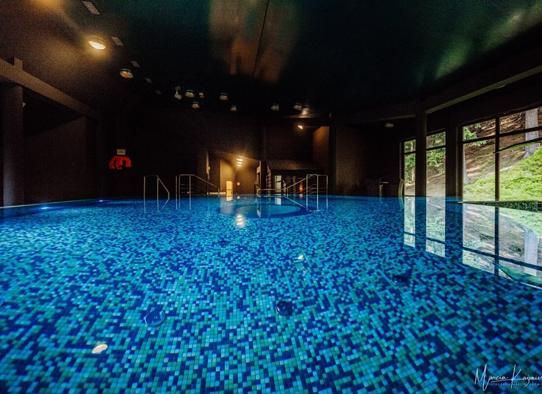Großer Innenhotelpool mit blauen Mosaikfliesen und großen Fenstern mit Blick auf einen grünen Wald.