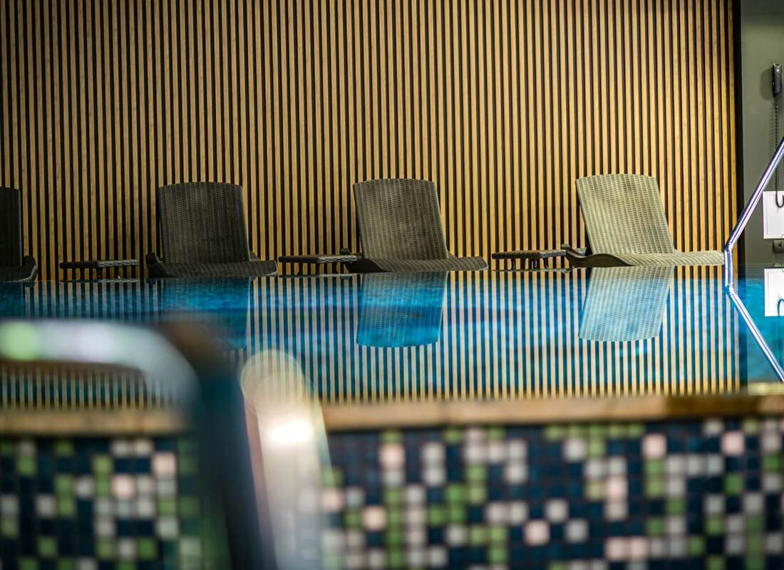 Moderner Innenpool mit schwarzem und grauem Liegestuhl vor einer Holzvertäfelung mit vertikalen Streifen