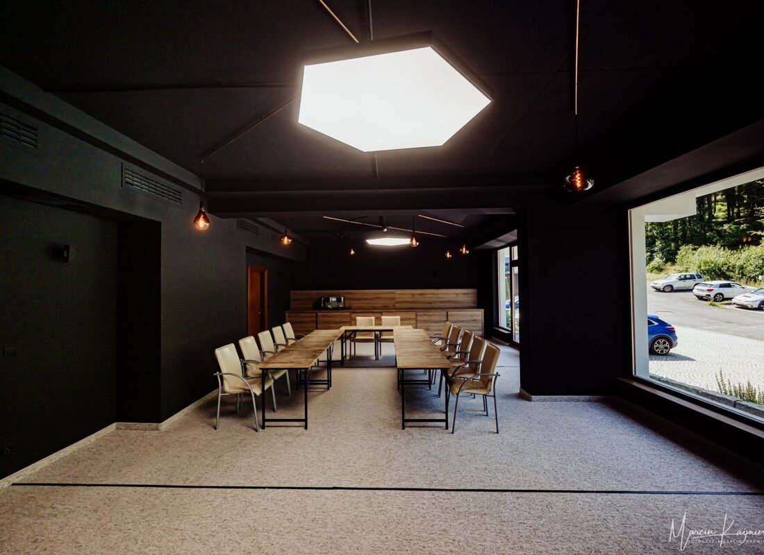 Moderner Konferenzraum mit hellem Deckenlicht, beigen Stühlen und großen Fenstern mit Blick auf Grünflächen und parkende Autos