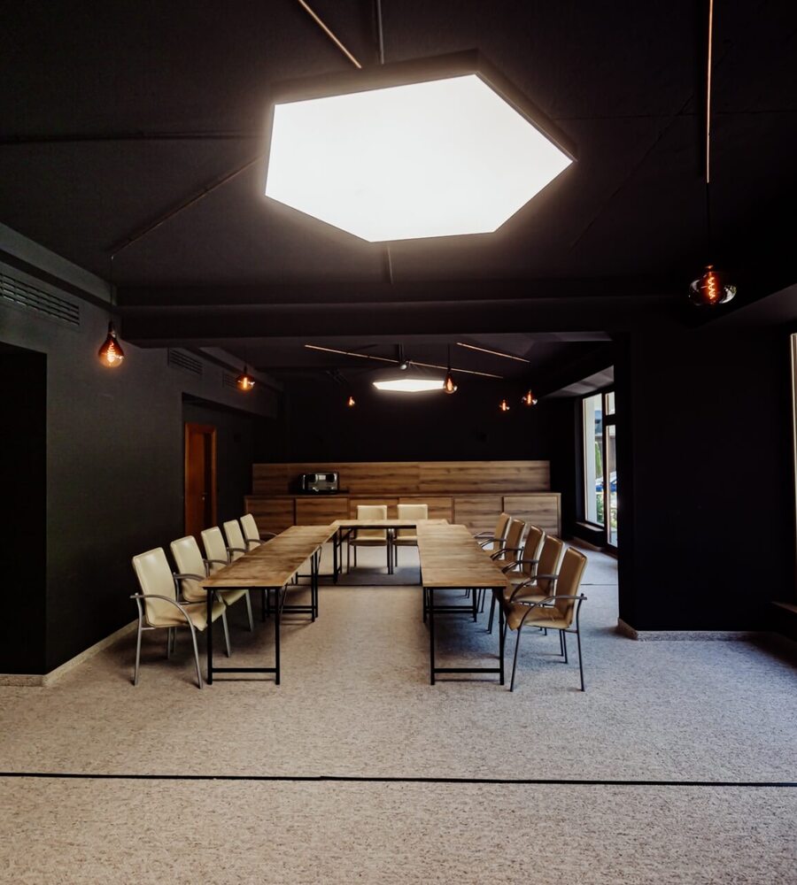 Nowoczesna sala konferencyjna z jasnym oświetleniem, beżowymi krzesłami i widokiem na zieleń za dużymi oknami