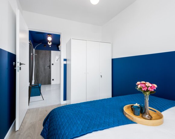 Modern hotel room with navy and white walls, blue bedspread, and a tray with flowers on the bed