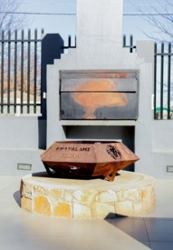 Outdoor fire pit with rusted metal bowl engraved Khayalami Ermelo, surrounded by stone base and concrete bench seating under clear sky