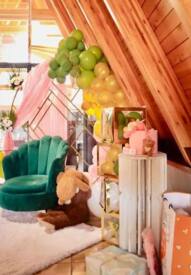 Cozy corner in a wooden loft with green velvet chair, plush bunny toy, pastel balloon decorations, and wrapped gifts on a fluffy rug