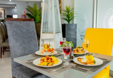 Modern dining table set with plated gourmet meals, assorted wines, and colorful upholstered chairs in bright restaurant ambiance