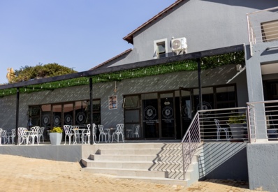 Hotel outdoor terrace with white modern chairs and tables under a shaded pergola with hanging lights, grey building facade