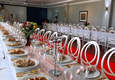 Elegant banquet room with long tables set for event, featuring gold utensils, beige napkins, crystal candle holders, and floral centerpieces