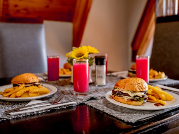 Cozy dining table set with cheeseburgers, seasoned fries, bright red drinks, and a sunflower centerpiece in a warm, wood-paneled room
