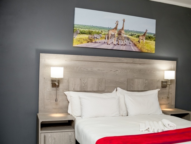 Modern hotel bedroom with king-size bed, white linens, wooden headboard, bedside lamps, and wildlife artwork above bed.