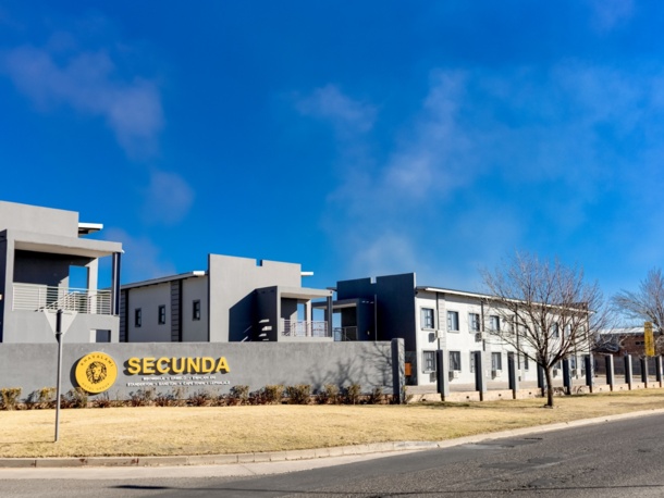 Modern hotel exterior with gray buildings, balconies, and signage for Secunda by Khayalami Hotel Group under a clear blue sky