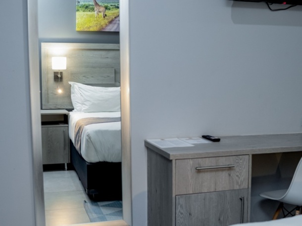 Modern hotel room with a neatly made bed reflected in a full-length mirror, featuring soft lighting and minimalist decor.
