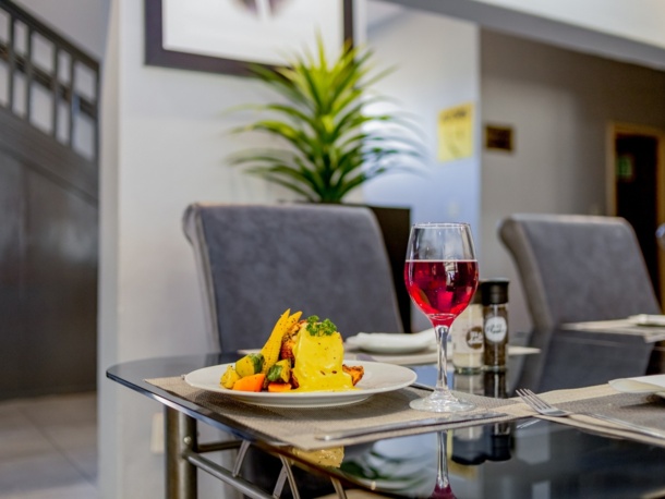 Modern dining table set with gourmet meal of vegetables and a creamy sauce, paired with a glass of red wine in elegant setting