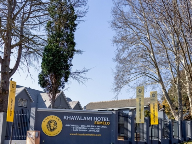 Exterior view of Khayalami Hotel Ermelo with clear signage, tall trees, and a calm, sunny atmosphere inviting guests.