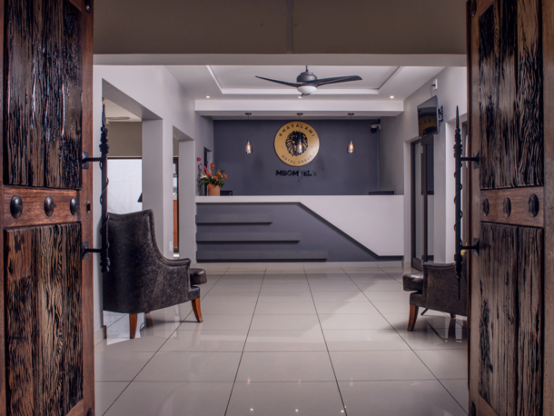Reception area with a modern white desk, gray accent wall, pendant lights, dark armchairs, and rustic wooden doors open