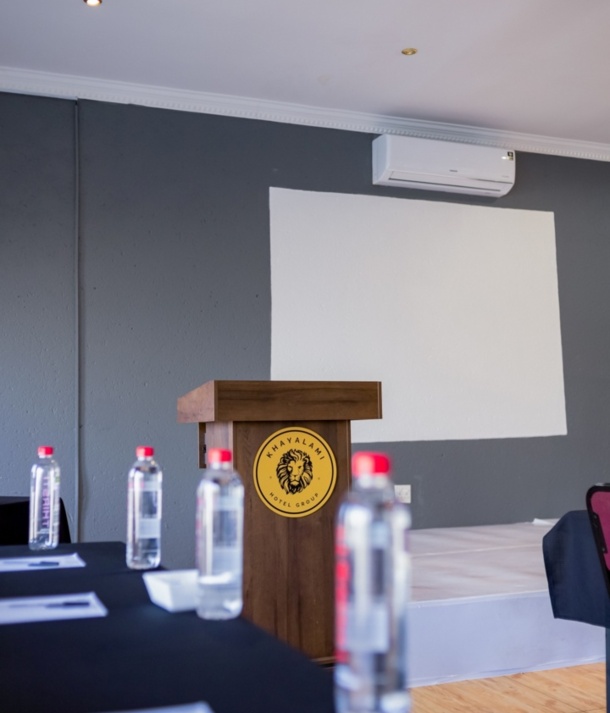 Conference room with wooden podium, branded with lion logo, water bottles on tables, and white projection screen on gray wall
