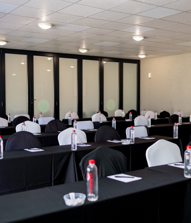 Modern meeting room with black-covered tables and alternating black and white chairs, each set with bottled water, notepads, and pens