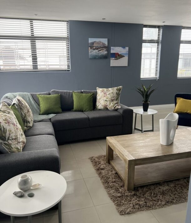Modern hotel lounge with gray sectional sofa, floral and green pillows, wood coffee table on shag rug, and natural light from large windows