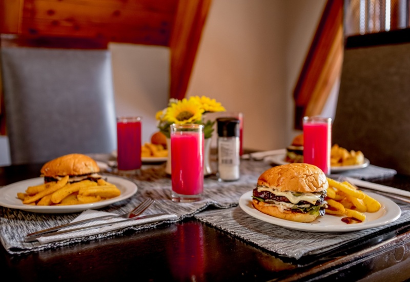 Cozy dining table set with cheeseburgers, seasoned fries, bright red drinks, and a sunflower centerpiece in a warm, wood-paneled room