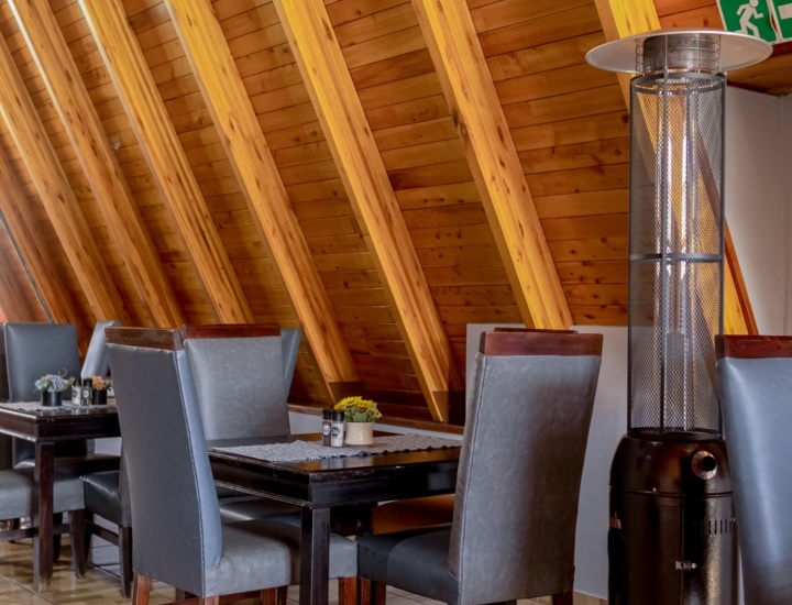 Cozy dining area with dark wood tables, gray padded chairs, wood-paneled sloped ceiling, and a standing patio heater nearby